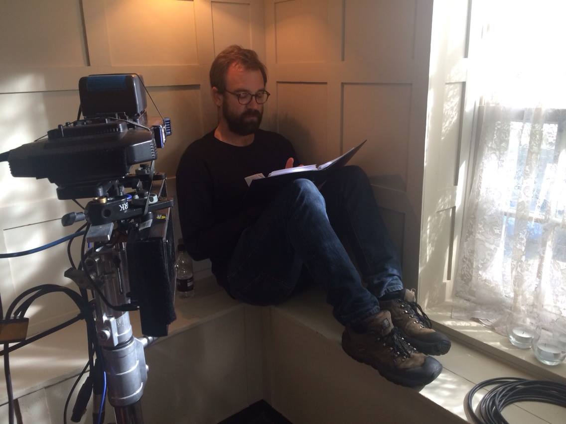 Director Adam Miller sits on a window sill reading his notes.