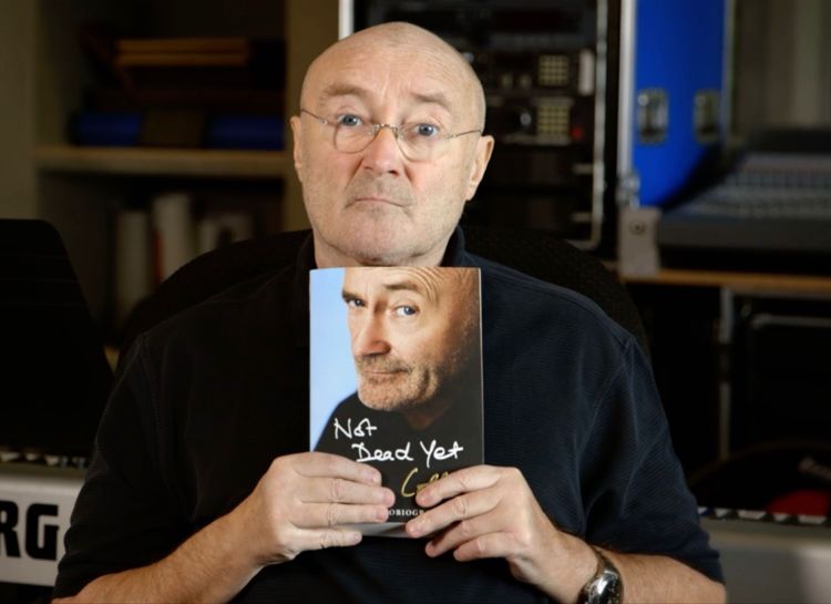 Phil Collins holds a copy of his autobiography in a recording studio