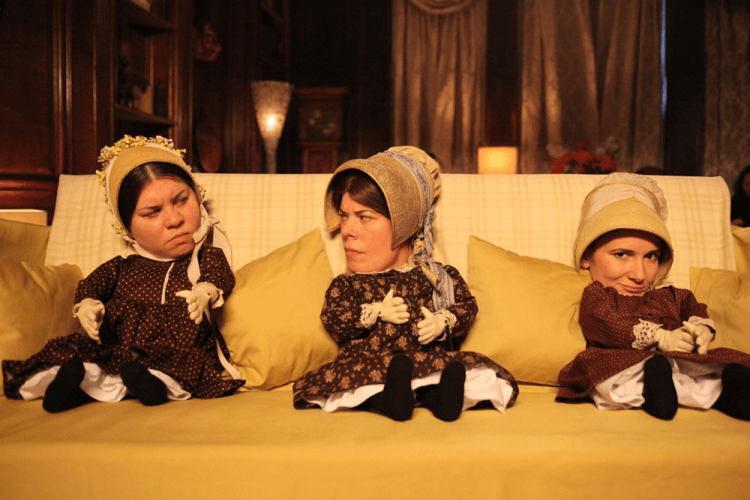Katy Brand, Selina Griffiths & Sarah Solemani as The Bronte Sisters - all three women are sticking their heads through holes in a sofa. In front of them are three tiny puppet bodies, making them look like small children.